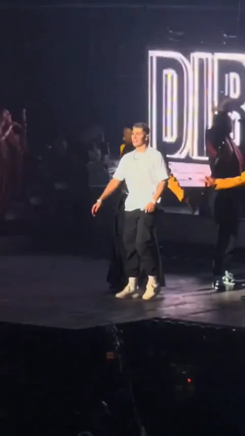 A man in a white tee and black joggers leads the backup crew under a spotlight on a concert stage